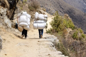 Two Sherpa Porters Carrying Heavy Sacks In The Himalaya At Evere
